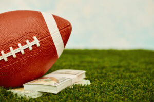 American football on turf with a wad of one hundred dollar bills. Fantasy sports betting concept