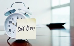 A clock with tax time sticky note and calculator on the desk