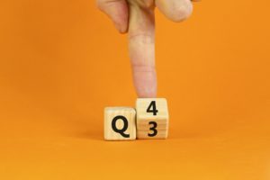 From 3rd to 4th quarter symbol. Businessman turns a wooden cube and changes words 'Q3' to 'Q4'. Beautiful orange table, orange background. Business, happy 4th quarter Q4 concept, copy space.