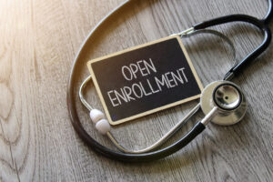 Stethoscope and chalkboard with text OPEN ENROLLMENT on wooden table. Medical and healthcare concept