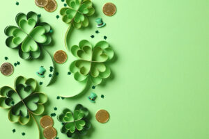St Patrick's Day holiday card. Flat lay four leaf clover paper art, gold coins, confetti on green background.