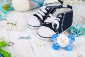 Baby first sneakers and dummy on floral wood background. Little baby shoes. Child planning. Pregnancy concept. Baby boy first steps. Waiting for a baby.