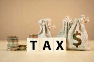 Tax wording on wooden cubes with US dollar coins and bag.