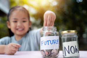 Little Asian girl saving money in Future bottle and now bottle , learning about saving, Kid save money for the future. Money, finances, insurance, and people concept.