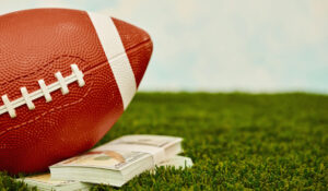 American football on turf with a wad of one hundred dollar bills. Fantasy sports betting concept