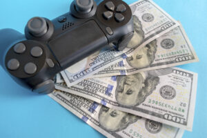 Black game joystick with us dollars on blue background. Playing for money concept. Game pad with money.