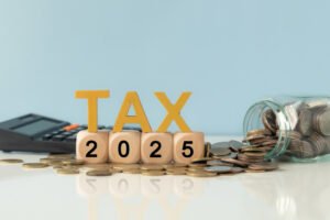 Business and tax concept. Wooden blocks spelling out TAX 2025, surrounded by coins and a calculator.  Tax deduction planning. Financial research, government taxes and calculation tax return.