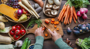 Woman chopping carrots on a table full of healthy Autumnal fruits and vegetables. Fresh organic seasonal produce background. Healthy vegetarian raw food. Food that boost the body inmune system. Nutrition and wellness, healthy diet and vegetable choice. Woman chopping carrots on a table full of healthy Autumnal fruits and vegetables. Fresh organic seasonal produce background. Healthy vegetarian raw food. Food that boost the body inmune system. Nutrition and wellness, healthy diet and vegetable choice. Overhead view