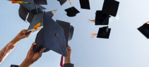 Cropped Hands Of People Throwing Mortarboards Against Clear Sky