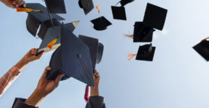 Cropped Hands Of People Throwing Mortarboards Against Clear Sky