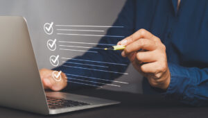 Quality control assurance of the ISO concept. A businessman in a navy blue shirt using an electronic pen to tick the correct sign mark in an online document checklist while sitting at the desk